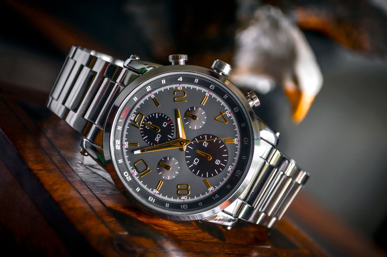 our-story Luxury wristwatch with stainless steel bracelet displayed elegantly on a wooden background.